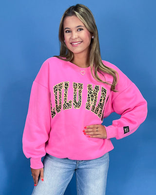 Woman wearing a pink sweatshirt with leopard print letters against a blue background