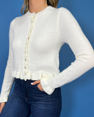 Ivory knit cardigan with ruffle trim, pearl-style buttons, ruffled hem, and feminine flared cuffs