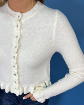Ivory knit cardigan with ruffle trim, pearl-style buttons, ruffled hem, and feminine flared cuffs