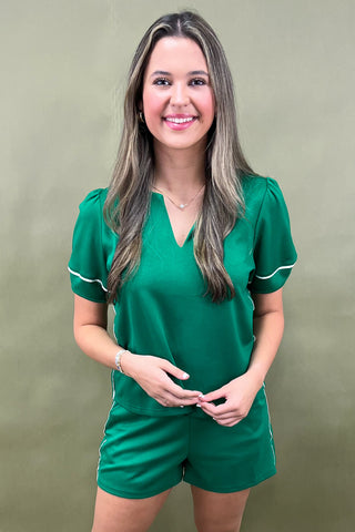 Woman wearing a green outfit with white trim against a beige background
