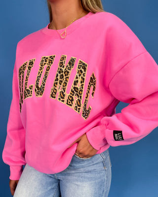 Person wearing a pink sweatshirt with leopard print text on a blue background