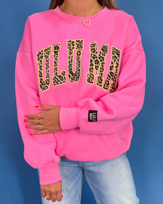 Person wearing a pink sweatshirt with 'OLUMI' in leopard print on a blue background