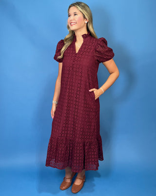 A woman modeling a burgundy eyelet midi dress with puff sleeves, a split neckline, and a ruffled hem