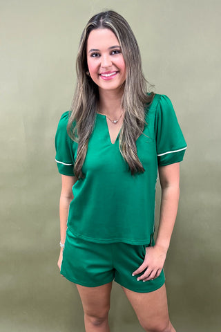 Woman wearing a green outfit with white trim against a beige background