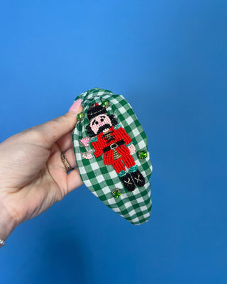 Shop the Green Gingham Nutcracker Headband at All About You Boutique! Festive Christmas hair accessory with beaded nutcracker, green rhinestones, and knotted top.