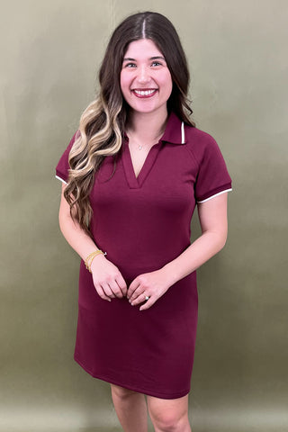 Woman wearing a maroon dress with white trim against a plain background