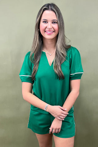 Woman wearing a green outfit with white trim against a beige background