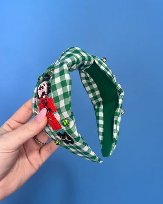 Shop the Green Gingham Nutcracker Headband at All About You Boutique! Festive Christmas hair accessory with beaded nutcracker, green rhinestones, and knotted top.