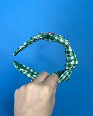 Shop the Green Gingham Nutcracker Headband at All About You Boutique! Festive Christmas hair accessory with beaded nutcracker, green rhinestones, and knotted top.