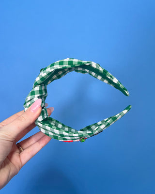 Shop the Green Gingham Nutcracker Headband at All About You Boutique! Festive Christmas hair accessory with beaded nutcracker, green rhinestones, and knotted top.