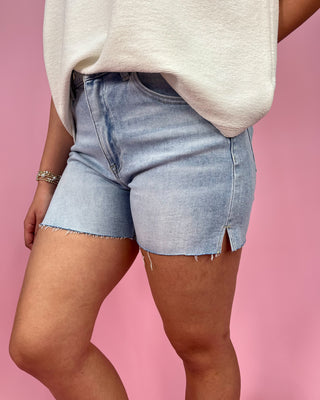 Person wearing light blue denim shorts and a beige top on a pink background