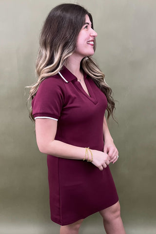 Woman wearing a maroon dress with a white collar against a green background