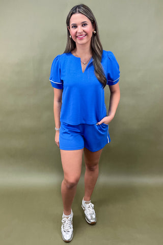 Woman wearing a blue outfit with white trim against a green background