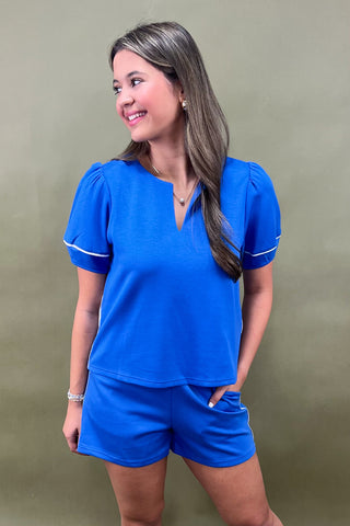 Woman wearing a blue outfit with white trim against a green background