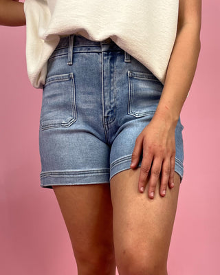 Person wearing light blue denim shorts on a pink background