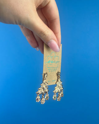 Shop the Christmas Tree Earrings at All About You Boutique! Festive gold-tone holiday earrings with pearl accents, sparkling stars, and dangling gift charms.