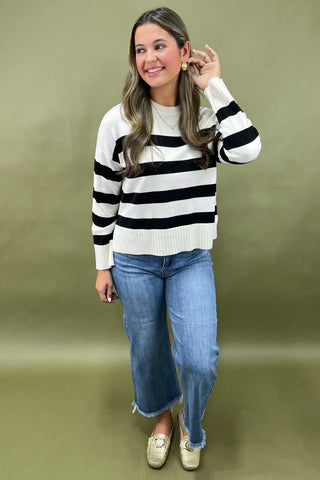 Woman wearing a black and white striped sweater and blue jeans on a green background