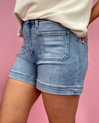 Person wearing light blue denim shorts on a pink background