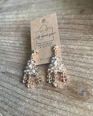 Shop the Christmas Tree Earrings at All About You Boutique! Festive gold-tone holiday earrings with pearl accents, sparkling stars, and dangling gift charms.