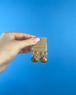 Shop the Holiday Ornament Bow Accent Earrings at All About You Boutique! Sparkling silver bows and red and green glitter ornaments bring festive Christmas charm.
