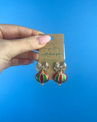 Shop the Holiday Ornament Bow Accent Earrings at All About You Boutique! Sparkling silver bows and red and green glitter ornaments bring festive Christmas charm.