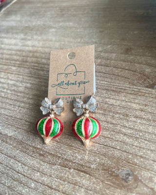 Shop the Holiday Ornament Bow Accent Earrings at All About You Boutique! Sparkling silver bows and red and green glitter ornaments bring festive Christmas charm.
