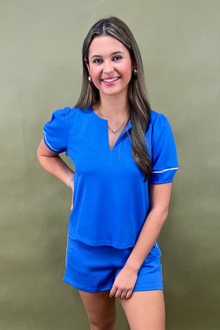 Woman wearing a blue outfit with white trim against a green background
