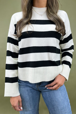 Person wearing a black and white striped sweater with blue jeans on a green background