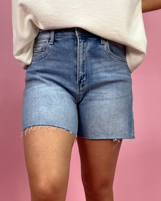 Person wearing blue denim shorts and a beige top against a pink background
