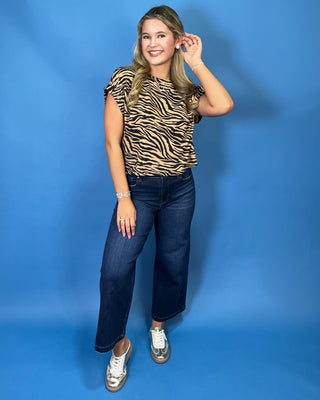 A woman modeling a short-sleeve tiger-print top and dark blue cropped jeans