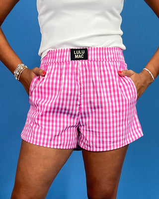 Person wearing pink checkered shorts with Lulu Mac label against a blue background