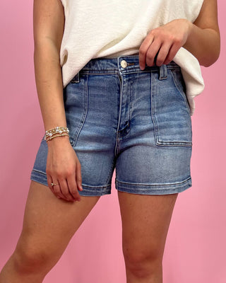Person wearing blue denim shorts and a white top on a pink background