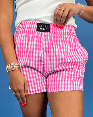 Person wearing pink checkered shorts with 'Lulu Mac' label against a blue background
