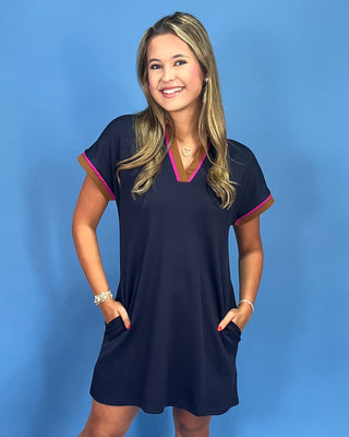 Woman wearing a navy dress with pink trim against a blue background