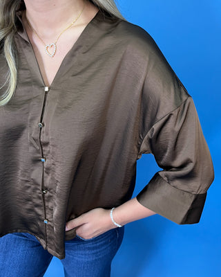 A woman wearing a brown satin button-up blouse with three-quarter sleeves and blue jeans