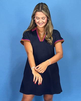 Woman wearing a navy dress with pink trim against a blue background