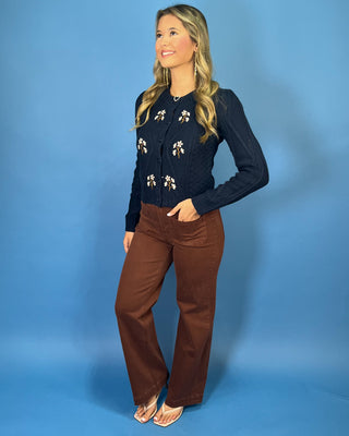 Navy cable knit cardigan with embroidered white daisies, button front, crew neckline, and long sleeves.