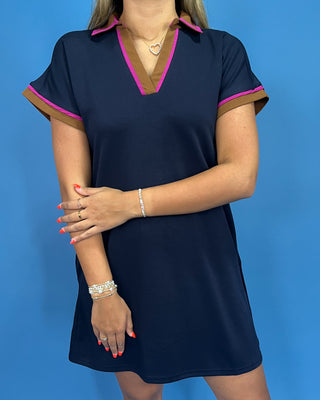 Woman wearing a navy dress with pink and brown trim against a blue background