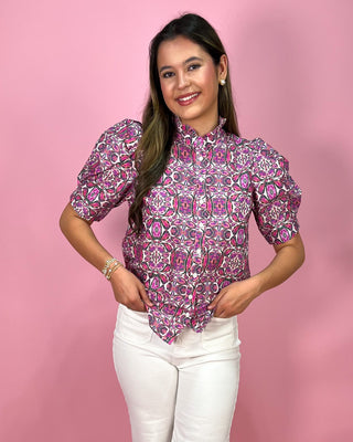 Woman wearing a patterned blouse and white pants against a pink background
