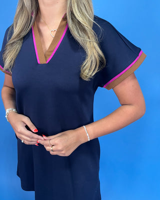 Woman wearing a navy blue top with pink trim against a blue background