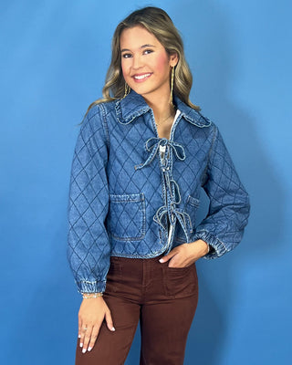 Quilted denim jacket with front tie closures, ruffle collar, patch pockets, and long sleeves.