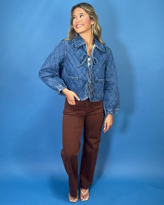 Quilted denim jacket with front tie closures, ruffle collar, patch pockets, and long sleeves.