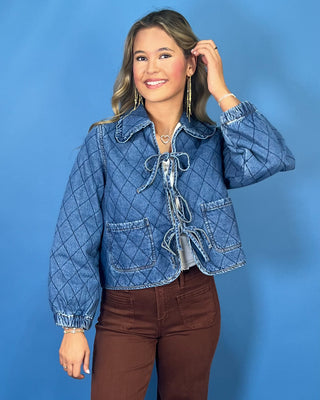 Quilted denim jacket with front tie closures, ruffle collar, patch pockets, and long sleeves.