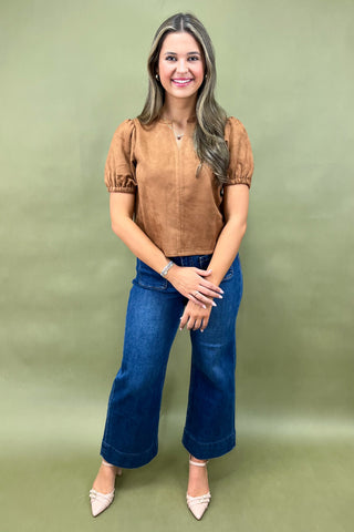 Woman wearing a brown top and blue jeans against a green background