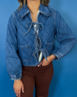 Quilted denim jacket with front tie closures, ruffle collar, patch pockets, and long sleeves.