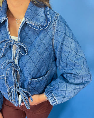 Quilted denim jacket with front tie closures, ruffle collar, patch pockets, and long sleeves.