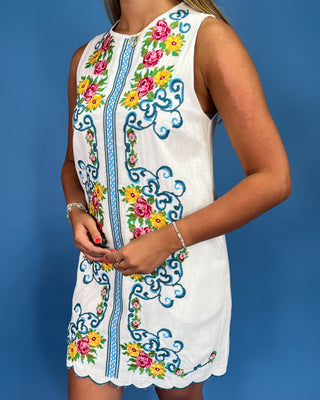 White sleeveless dress with colorful floral embroidery on a blue background