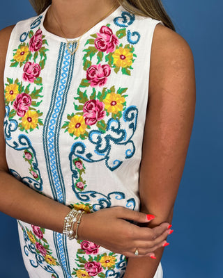 White sleeveless top with colorful floral embroidery on a blue background