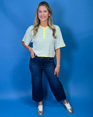 A woman modeling a short-sleeve striped henley shirt with dark blue cropped jeans and white sneakers
