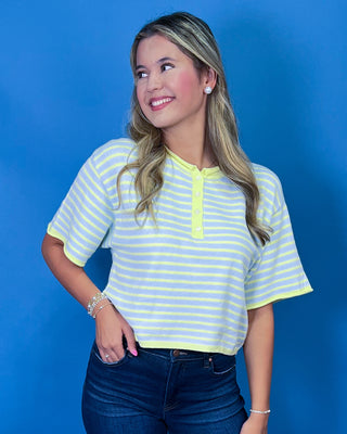 A woman wearing a short-sleeve henley top with light yellow and white horizontal stripes, paired with dark blue jeans